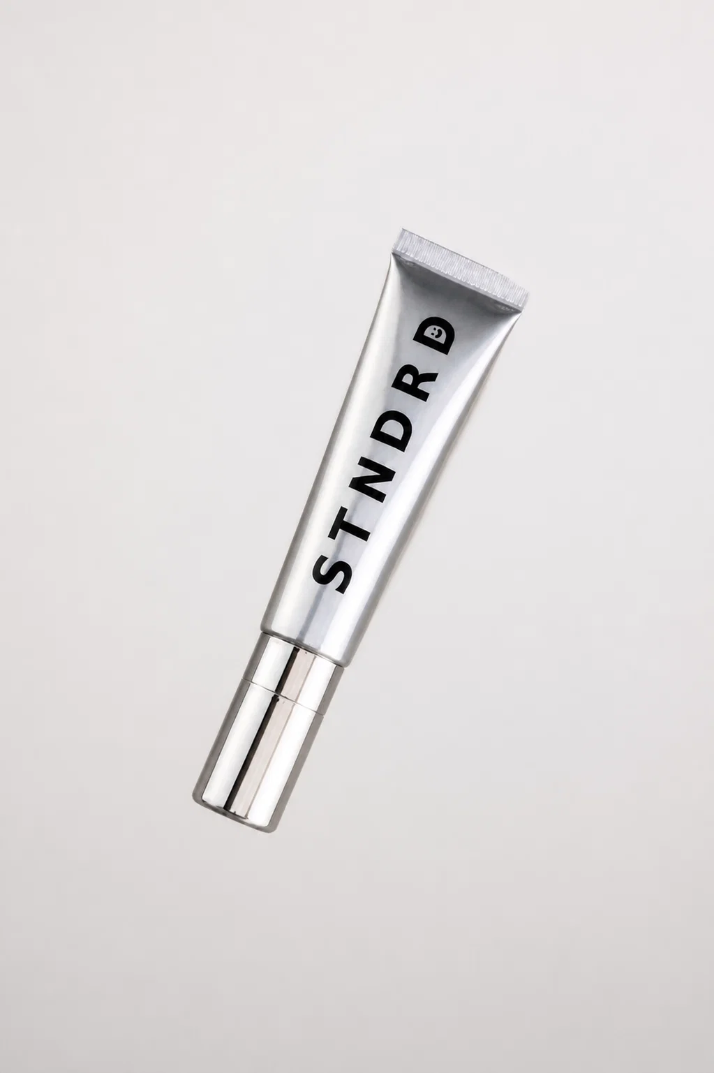 STNDRD lip balm tube lying at an angle on a light grey surface
